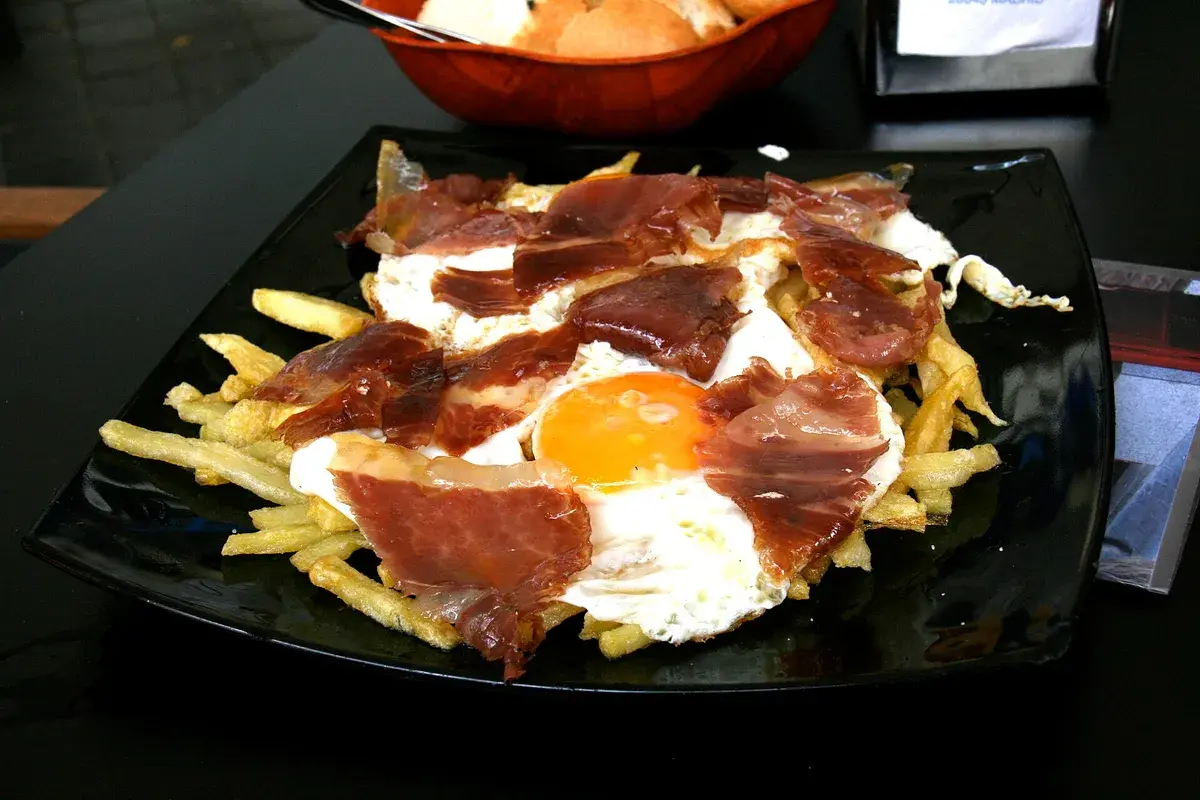 碎蛋土豆(Huevos rotos),火腿与炸土豆上盖着戳破的煎蛋,马德里酒吧的看家美味。摄影:Tamorlan,CC BY-SA 3.0